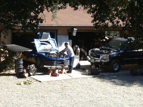 1995 Ford Probe - Two vehicles are being worked on outside a garage, one a blue car and the other a black GMC pickup truck.