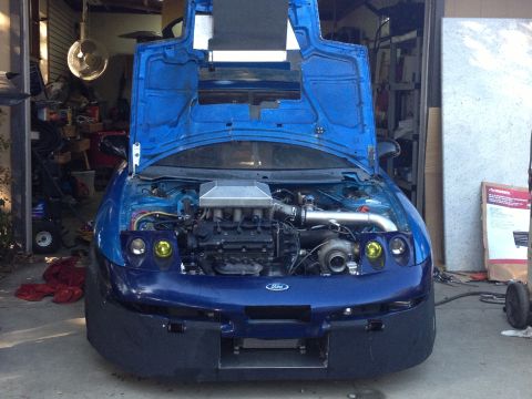 1995 Ford Probe - Front view of a blue car with its hood open, revealing the engine and a turbocharger. A Ford badge is visible on the grille.
