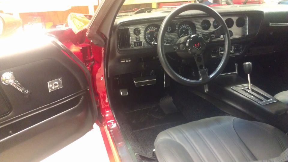 Interior shot of a red car, showing the dashboard, steering wheel with a bird emblem, center console with automatic shifter, and part of the driver's seat