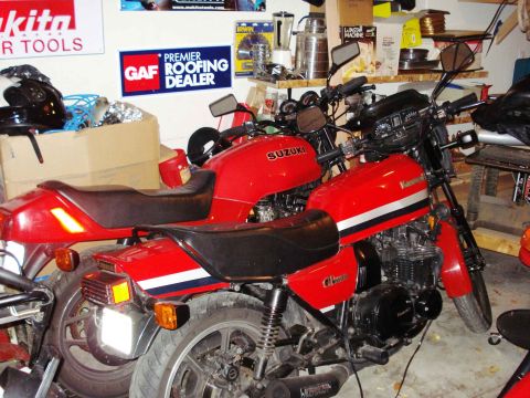 2008 Ford Crown Victoria - Two red motorcycles, a Suzuki and a Kawasaki, are parked in a garage with various tools and signs on the wall.