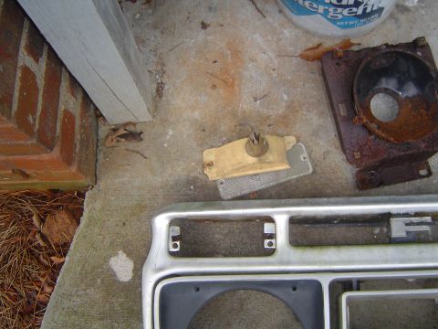 1986 Ford Bronco - Parts from a Ford Bronco, including a chrome grille and a rusty headlight assembly, lie on the ground.