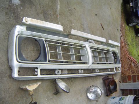 1986 Ford Bronco - A disassembled Ford grille, likely from a 1970s truck, lies on the ground with various lights.