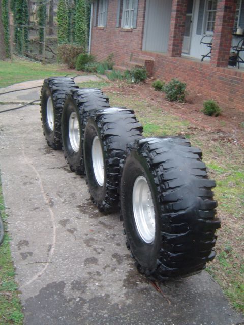 1986 Ford Bronco - Four oversized tires are lined up on a walkway next to a house.