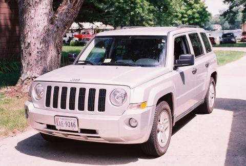 1971 Ford Ranchero - This silver Jeep Patriot is seen parked outdoors, with a tree to its left and other vehicles in the background.