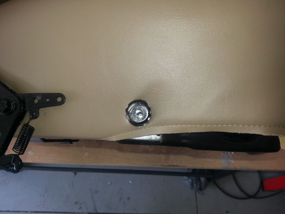 Close-up of a tan seat with a metal adjustment knob and spring mechanism