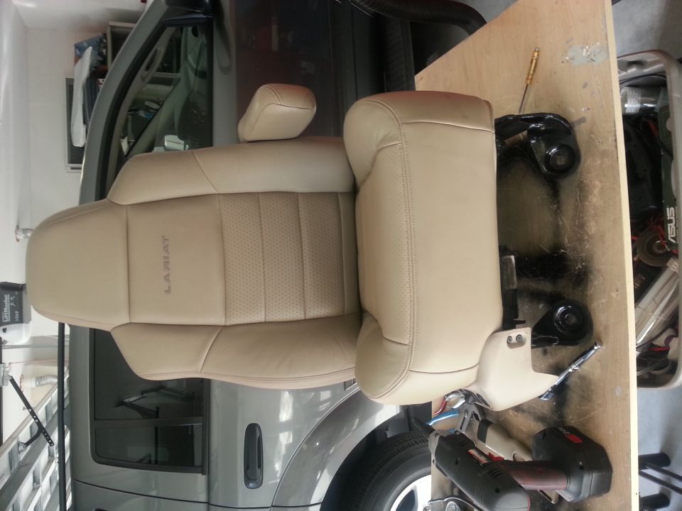 Tan leather car seat with 'Lariat' embossed on the side, mounted on a wooden board with hardware