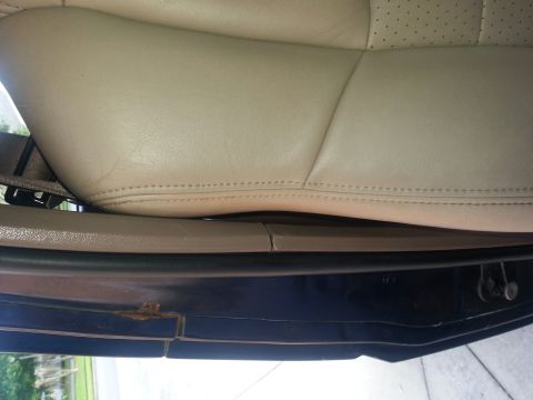 1994 Ford Bronco - The interior of a vehicle shows a tan leather seat and the door sill with visible rust.