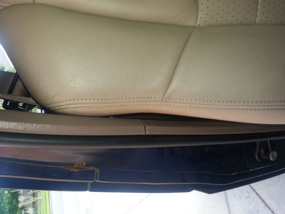 Close-up of a tan leather car seat and door sill. A seatbelt is visible. Some rust is present on the door sill