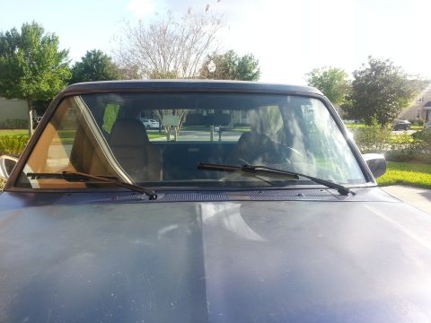 1994 Ford Bronco - Truck interior seen from the front, with windshield wipers visible. Exterior scenery is reflected.