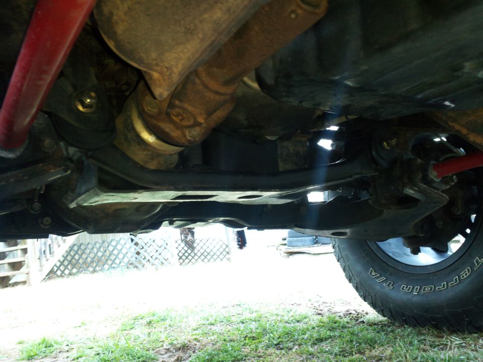 Undercarriage view of truck suspension and drivetrain components, with a tire visible