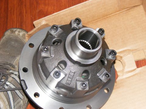 Close-up of a differential carrier with bolts and splines visible. A shoe is in the background