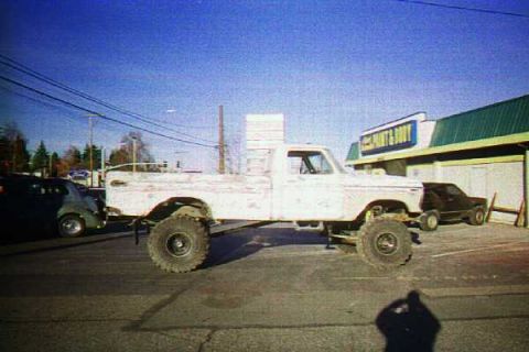1976 Ford F-150 - A modified pickup truck with large tires sits parked on asphalt in front of a building.