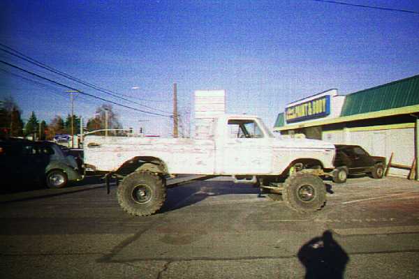 Lifted white Ford pickup on large mud tires parked in a street