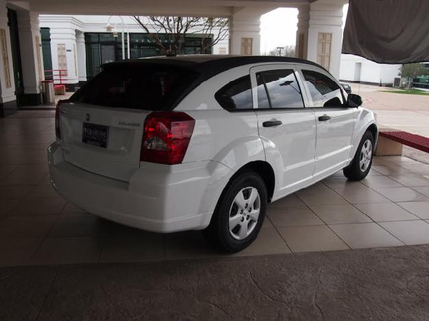 White hatchback car parked under an overhang, rear quarter view. License plate is visible