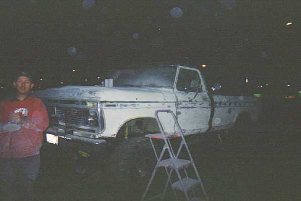 Lifted white 1970s Ford pickup photographed at night with a man nearby