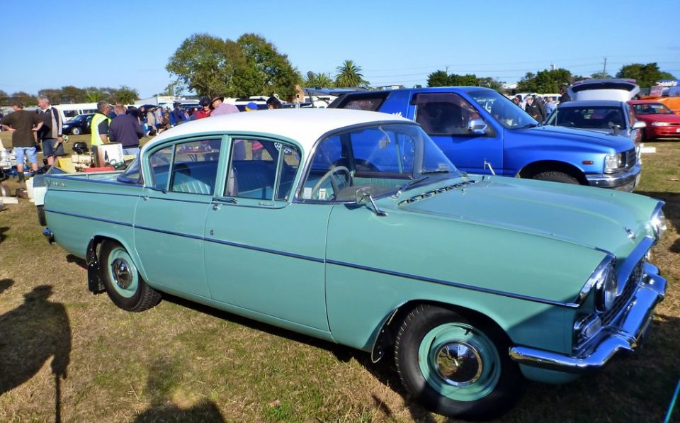 Turquoise and white sedan with chrome accents parked on grass, front quarter view