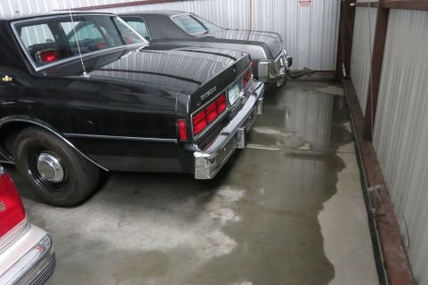 1991 Ford LTD Crown Victoria - Two cars are parked inside a metal building with a wet concrete floor.