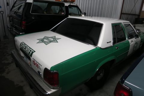1991 Ford LTD Crown Victoria - A white and green Sheriff's patrol car is parked indoors next to another vehicle.