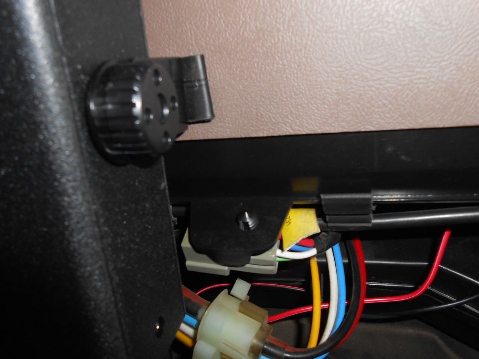 Close-up of vehicle interior wiring with a black knob and beige dashboard panel