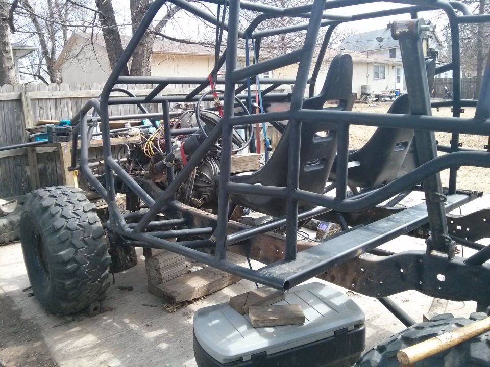 Custom off-road buggy frame with racing seats, engine, and large tires. Vehicle is on blocks