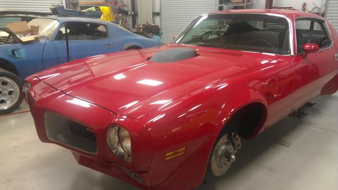 1972 Pontiac Trans Am - A red muscle car is in a garage, with another blue car behind it. The red car appears to be undergoing some work.