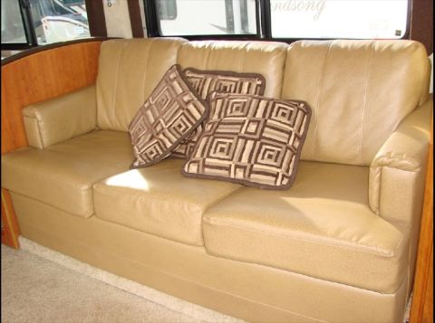 2010 Ford F-450 - Interior view of a tan leather sofa with decorative pillows, set against wood paneling and windows.