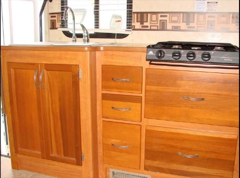 2010 Ford F-450 - The interior of an RV shows a kitchen counter with a sink, faucet, and a stove top above wooden cabinets and drawers.
