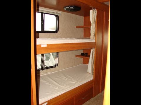 2010 Ford F-450 - This photo shows the interior of an RV, stacked bunk beds with white linens and wooden cabinetry.