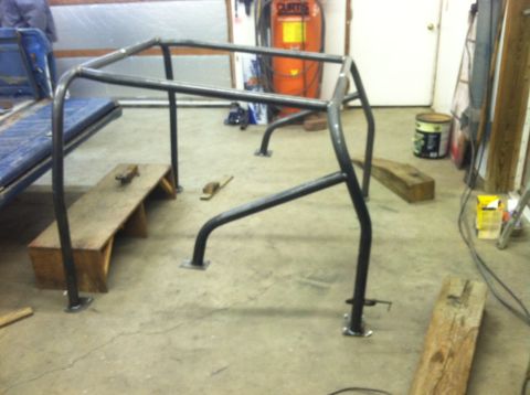 1979 Ford Bronco - A custom roll cage is being fabricated or installed in a garage setting, with a blue seat from a vehicle in the background.