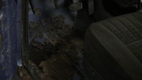 1979 Ford Bronco - The interior floor of the vehicle shows significant rust and damage, with a portion of the seat visible.