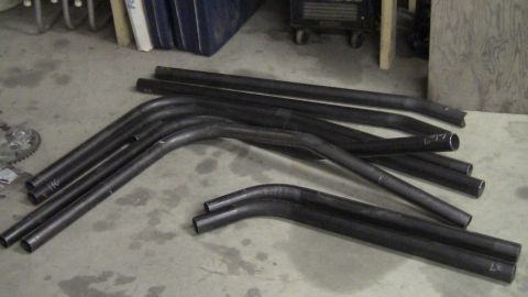 1979 Ford Bronco - Various pieces of black metal tubing are laid out on a concrete floor, some with bent sections.