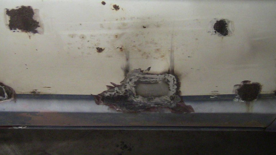 Close-up of a white vehicle panel with significant rust and holes, showing damage