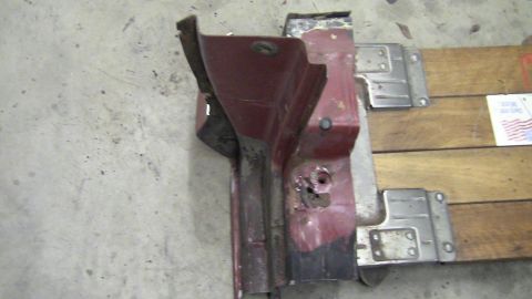 1979 Ford Bronco - A close-up view of a damaged red metal car part, possibly a fender or door section, with visible rust and mounting hardware.