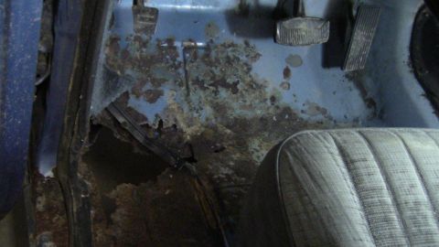 1979 Ford Bronco - The interior floor of a vehicle shows extensive rust and damage, with a portion of the seat visible.