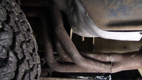 1979 Ford Bronco - Underside view of a vehicle's exhaust manifold and tire, with visible rust on the pipes.