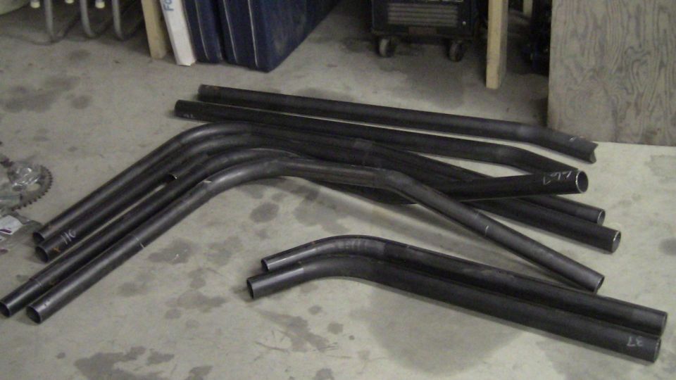 Pile of bent black metal tubes on a concrete floor. Some have markings
