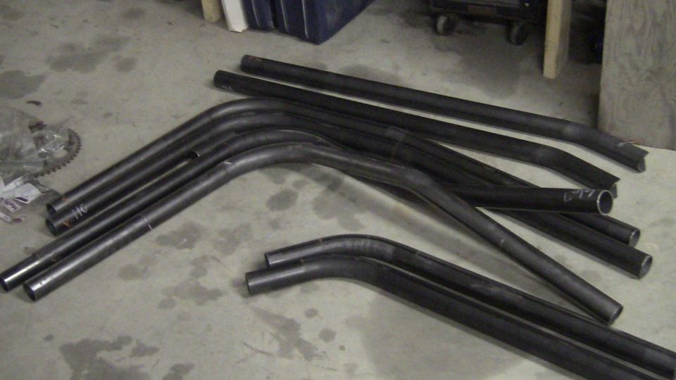 Metal tubes bent into various curves and straight sections lie on a concrete floor