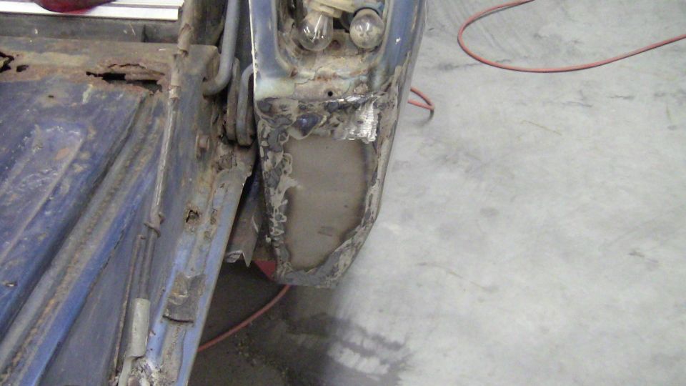 rusted blue vehicle body panel with exposed metal and light bulbs visible