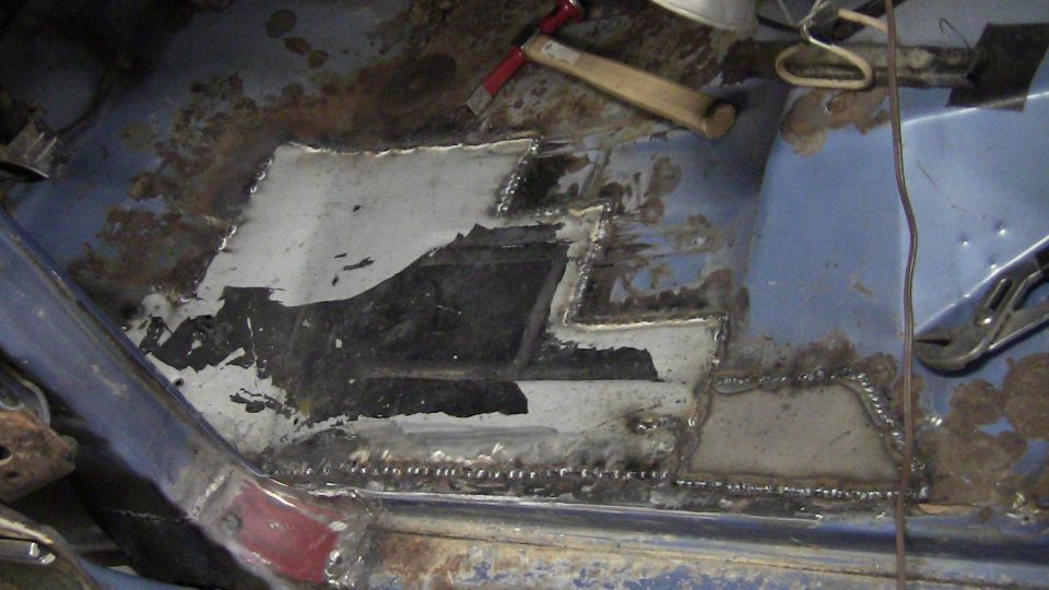 Vehicle floor with rust damage and new metal patches welded in place. A hammer and pliers are visible