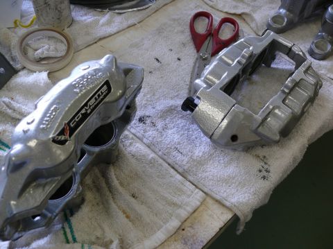 Two silver Corvette brake calipers, one with a CORVETTE STINGRAY badge, on a white towel with red scissors