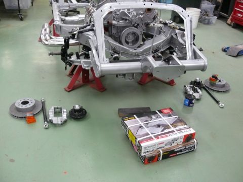Car frame on jack stands with brake rotors, calipers, and boxes of parts on the floor