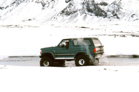 1996 Ford Bronco - A green 1996 Ford Bronco navigates a snowy landscape, kicking up dust from its large tires.