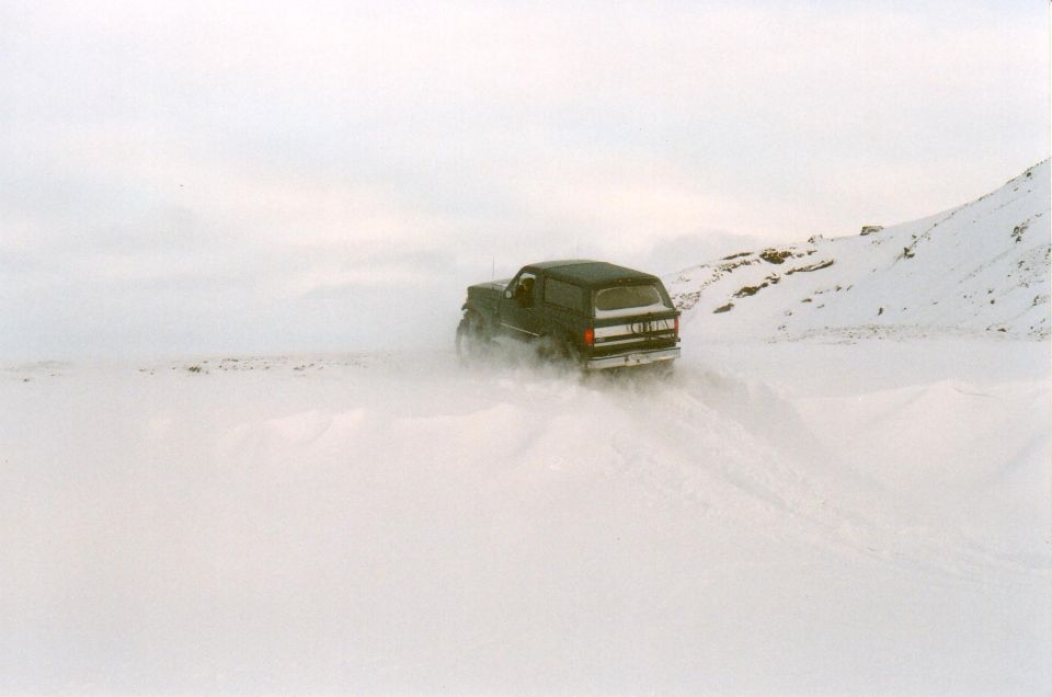 Dark Ford Bronco SUV driving through deep snow, spraying snow behind it
