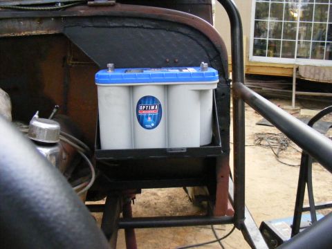 Optima battery in a black metal bracket, mounted in a vehicle's engine bay