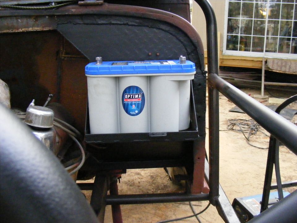 Optima battery in a black metal bracket, mounted in a vehicle's engine bay