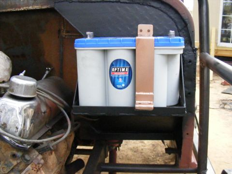 Optima battery with blue top and copper hold-down strap, mounted in a vehicle's engine bay