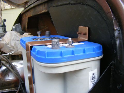Blue top car battery secured with copper bracket in engine bay