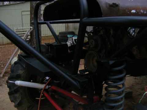 Off-road vehicle chassis with large tire, shock absorber, and exposed engine parts. Black roll cage visible