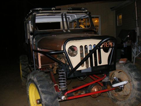 Custom off-road vehicle with large tires, roll cage, and a beige grille with 'FREAK' written on it