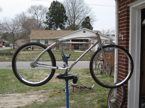 Chrome bicycle frame on repair stand, with another bicycle visible in background